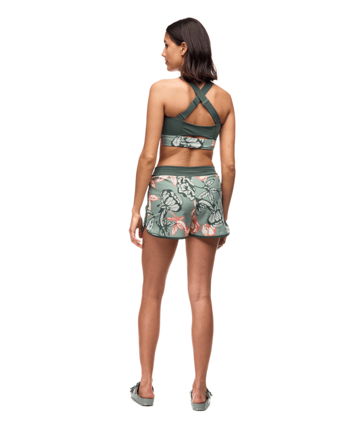 Woman wearing a green sports bra and shorts with floral pattern on a white background