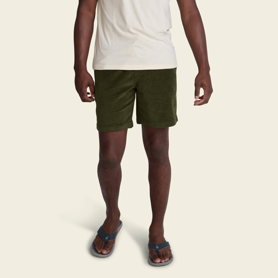 Person wearing green shorts and a white shirt on a beige background