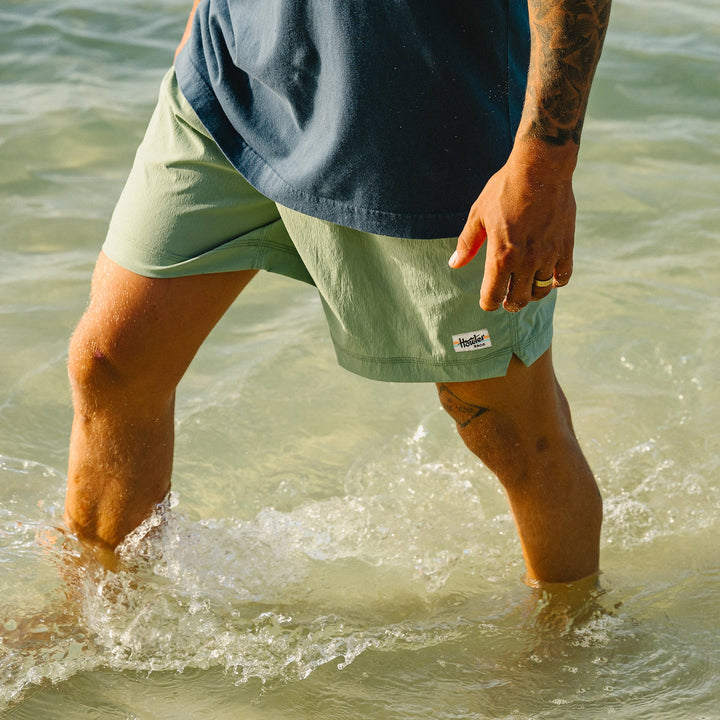 Person wearing light green shorts and a blue shirt standing in shallow water.