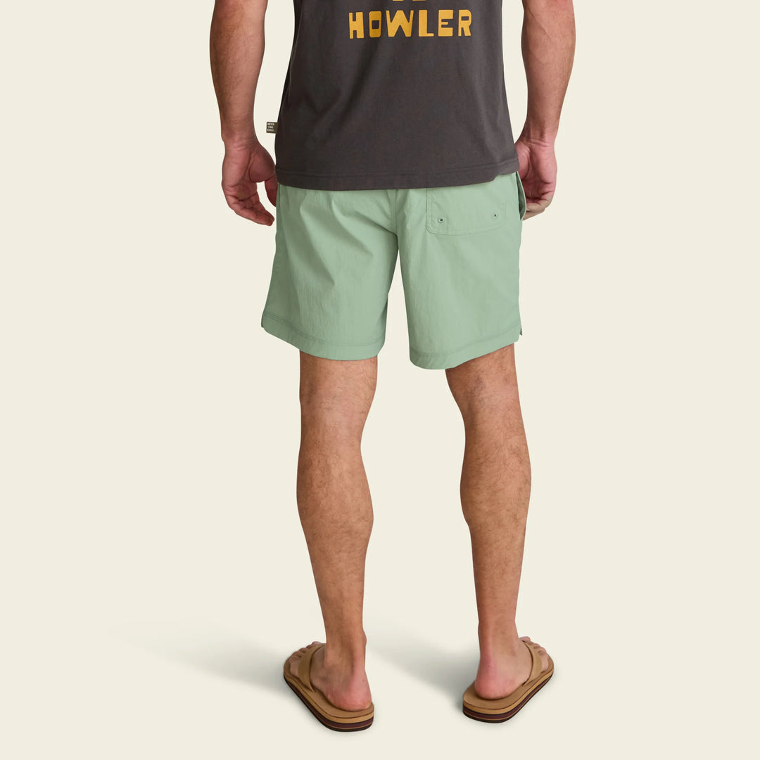Person wearing green shorts and a dark shirt with 'HOWLER' logo on a beige background