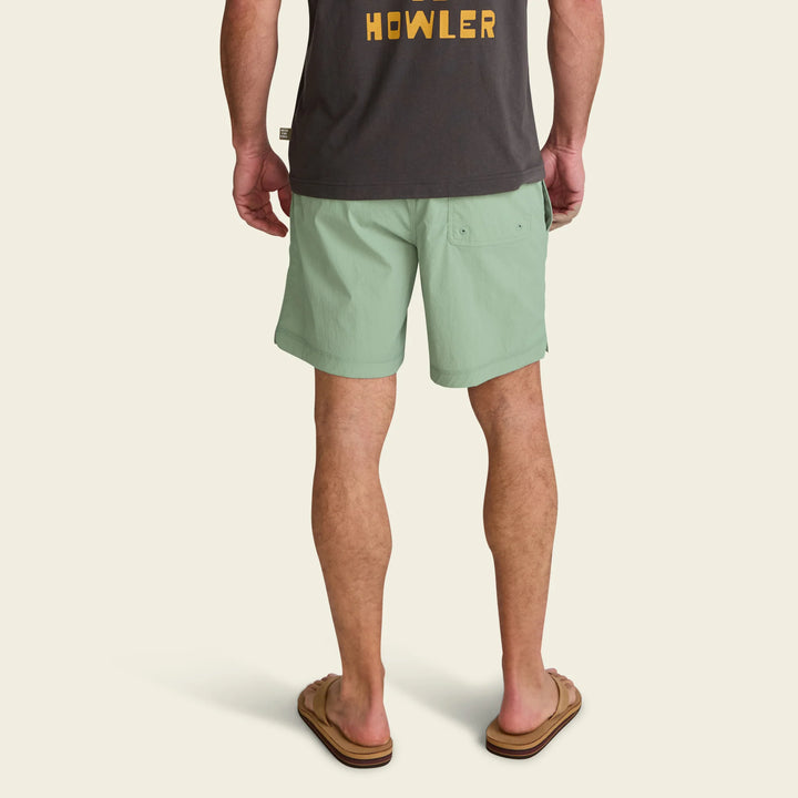 Person wearing green shorts and a dark shirt with 'HOWLER' logo on a beige background