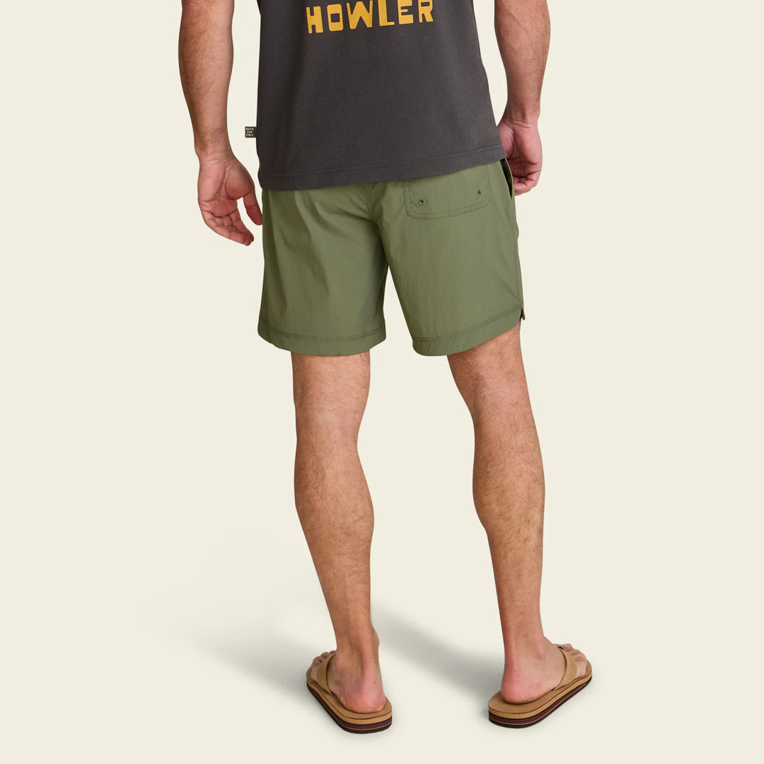 Person wearing green shorts and a dark shirt with 'Howler' branding on a beige background