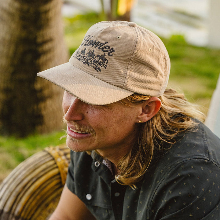 Man wearing a beige cap with a logo, sitting outdoors.