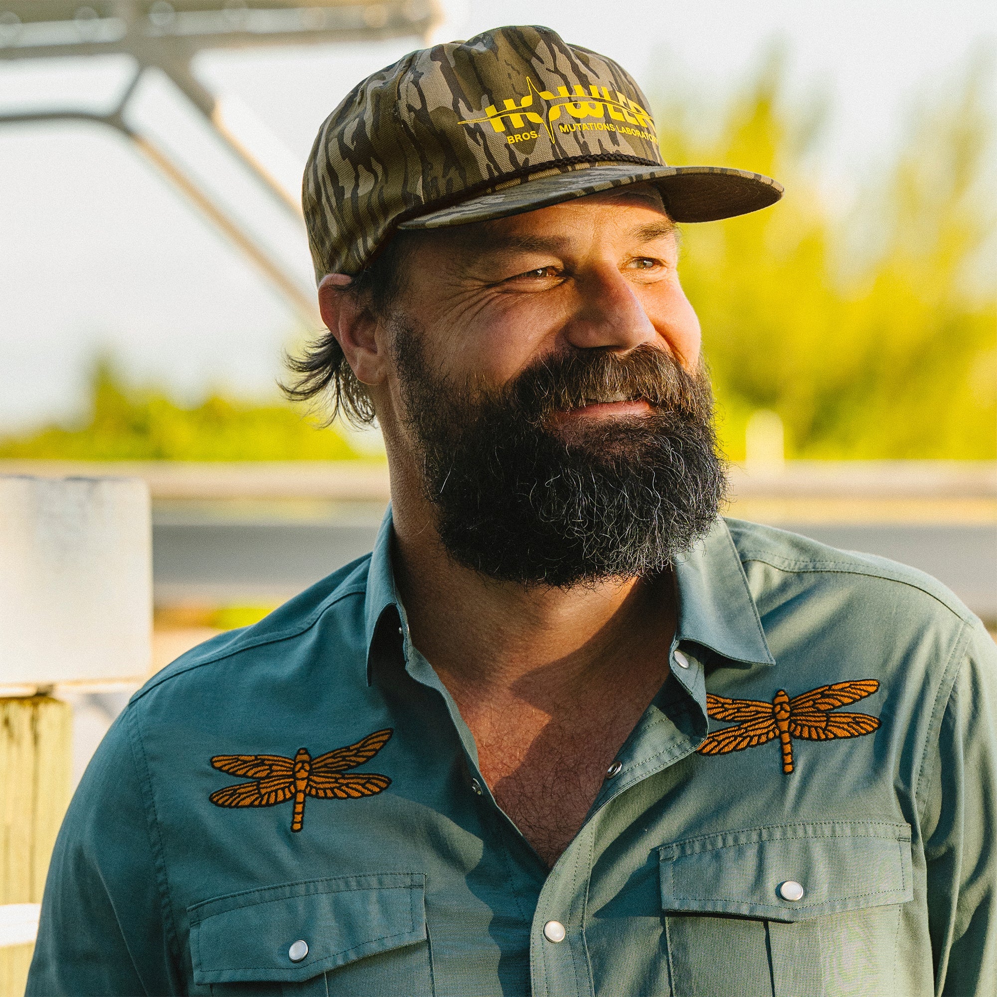 Man wearing a cap and shirt with dragonfly designs outdoors