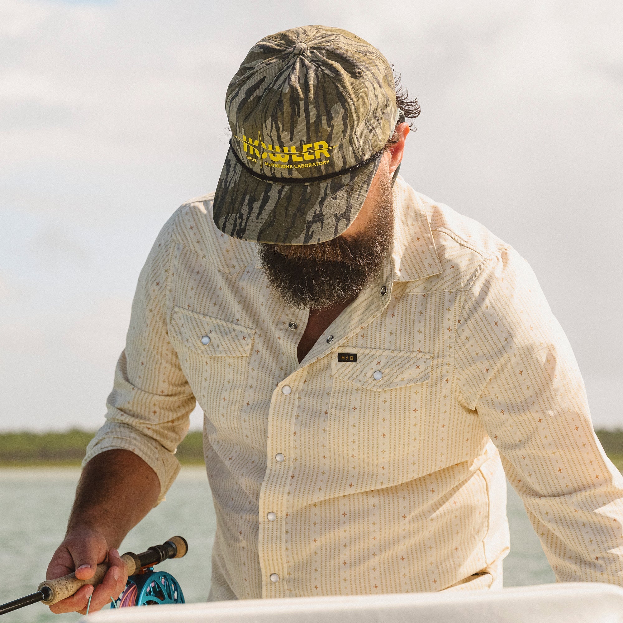 Man wearing a camouflage cap and beige shirt, holding a fishing rod on a boat.