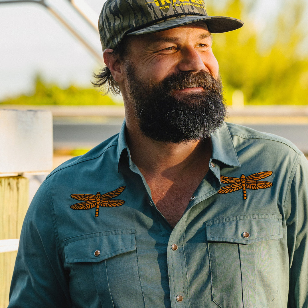 Man wearing a cap and shirt with dragonfly designs outdoors