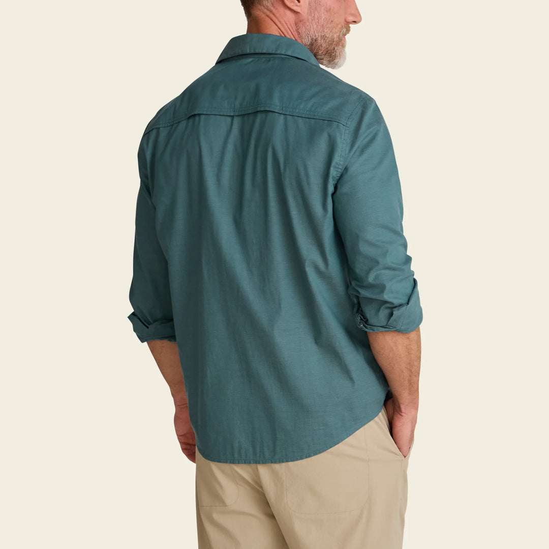 Man wearing a teal shirt and beige pants on a beige background