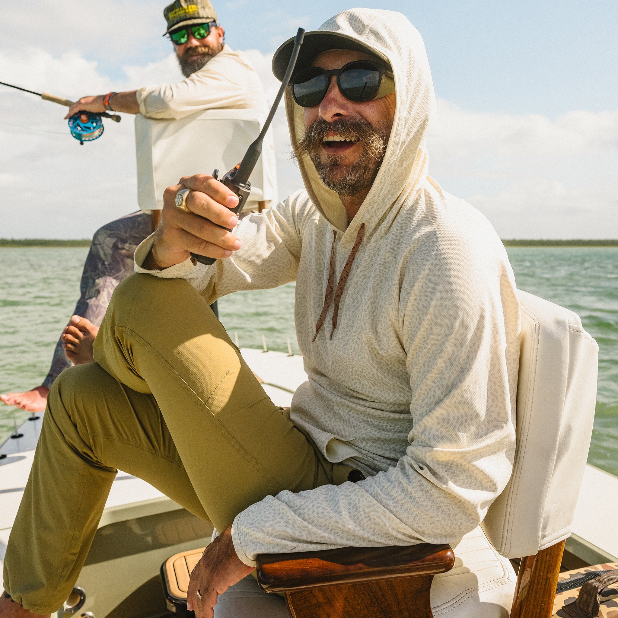 Two men on a boat in a body of water, one holding a fishing rod and the other using a walkie-talkie.
