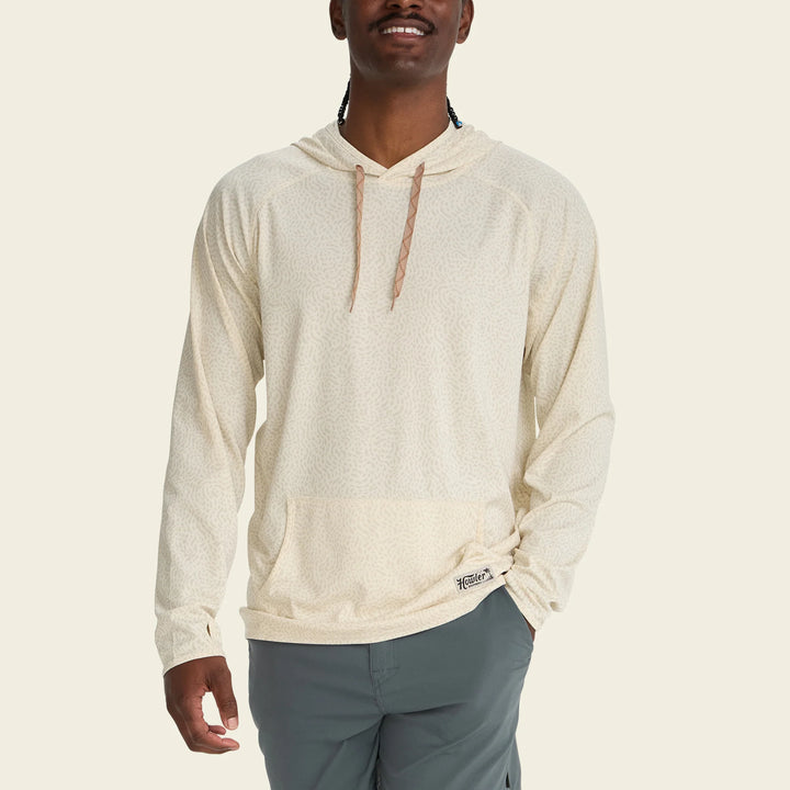 Man wearing a beige hoodie with a brand logo on a beige background