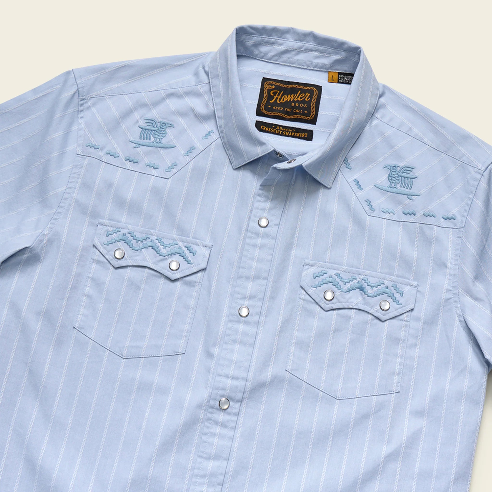 Light blue denim shirt with embroidered designs on a beige background