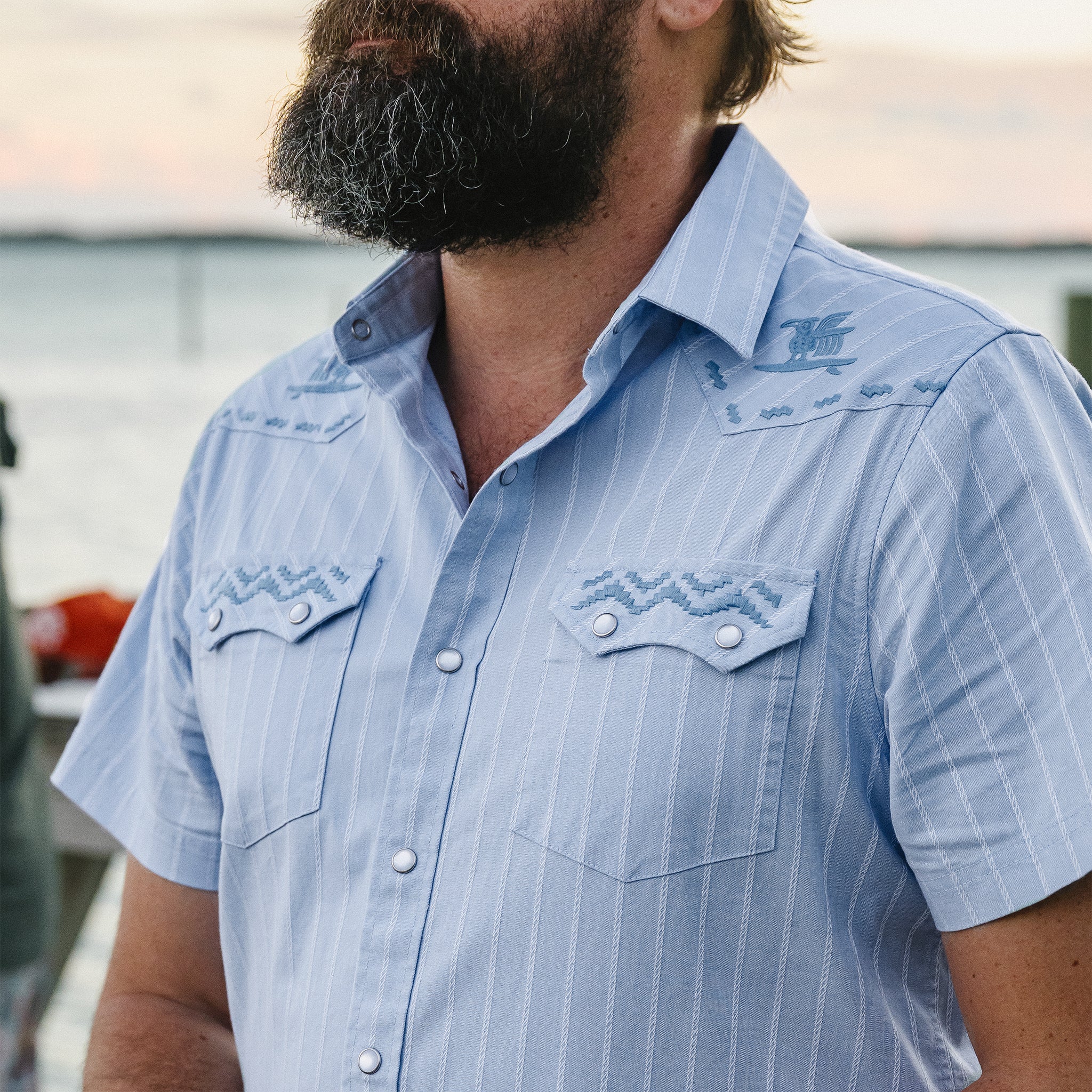 Man wearing a light blue striped shirt with a brand logo.