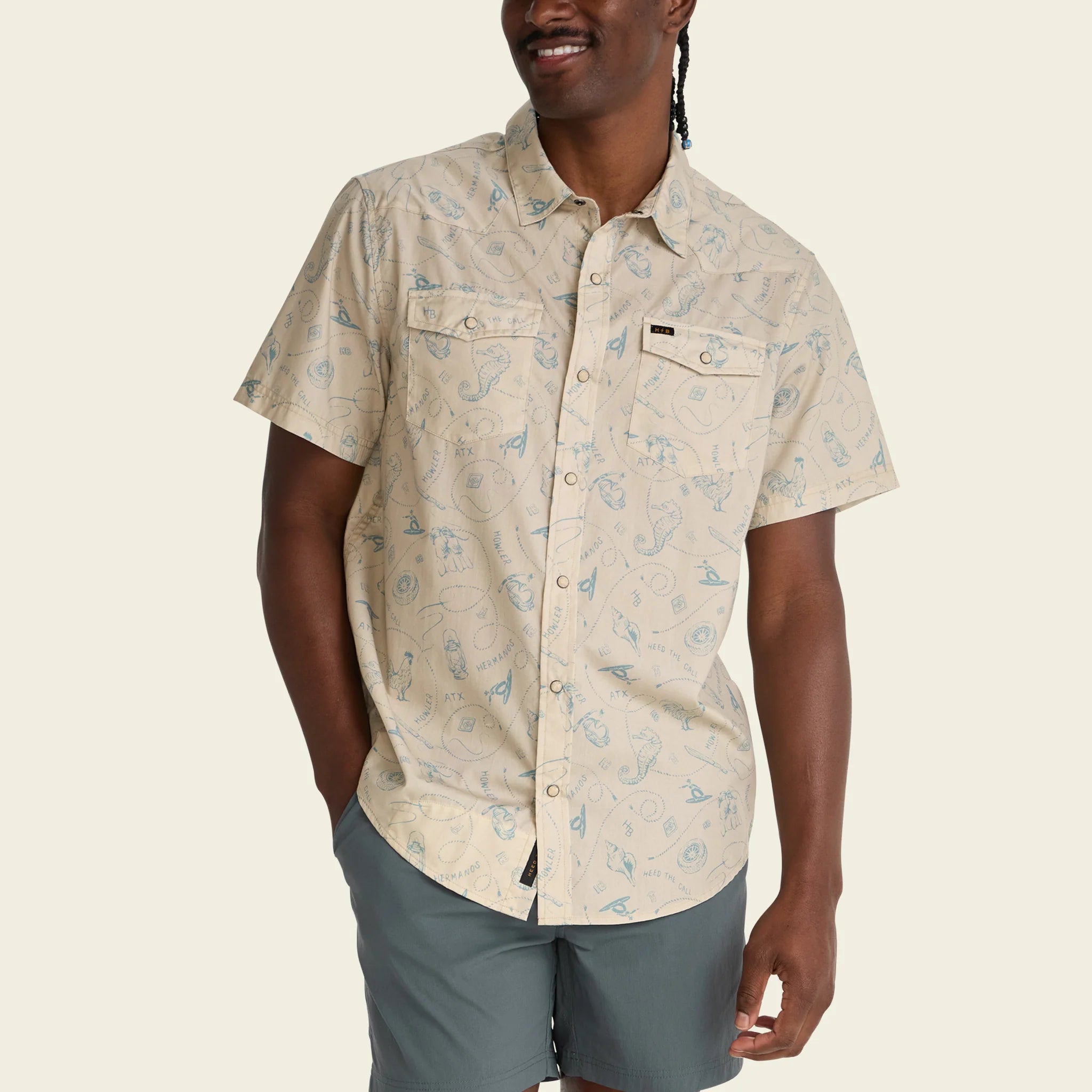 Man wearing a beige patterned shirt and gray shorts on a beige background