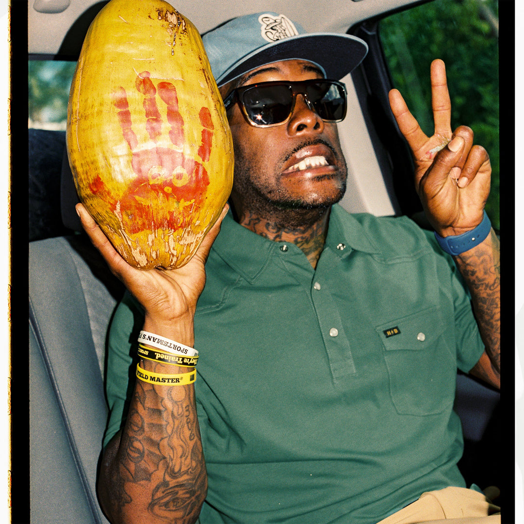 Person holding a large yellow fruit with a hand print, wearing sunglasses and a green shirt.