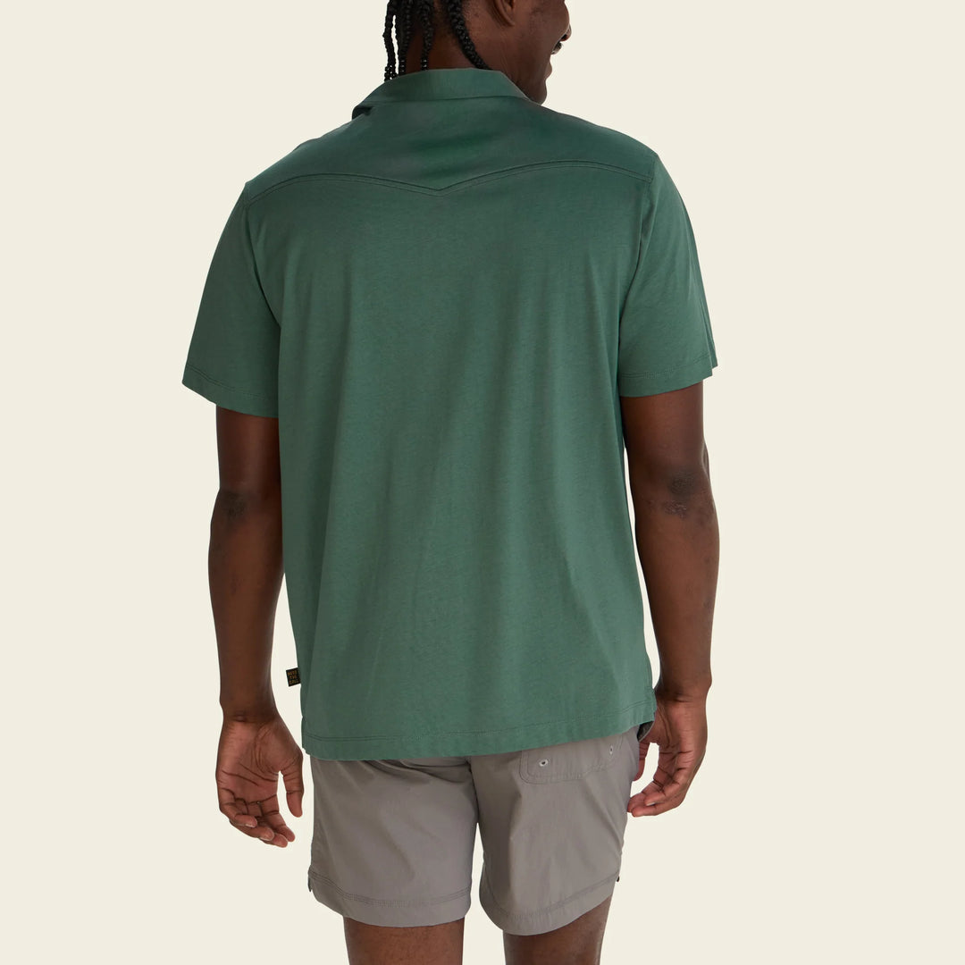 Person wearing a green polo shirt and beige shorts on a white background