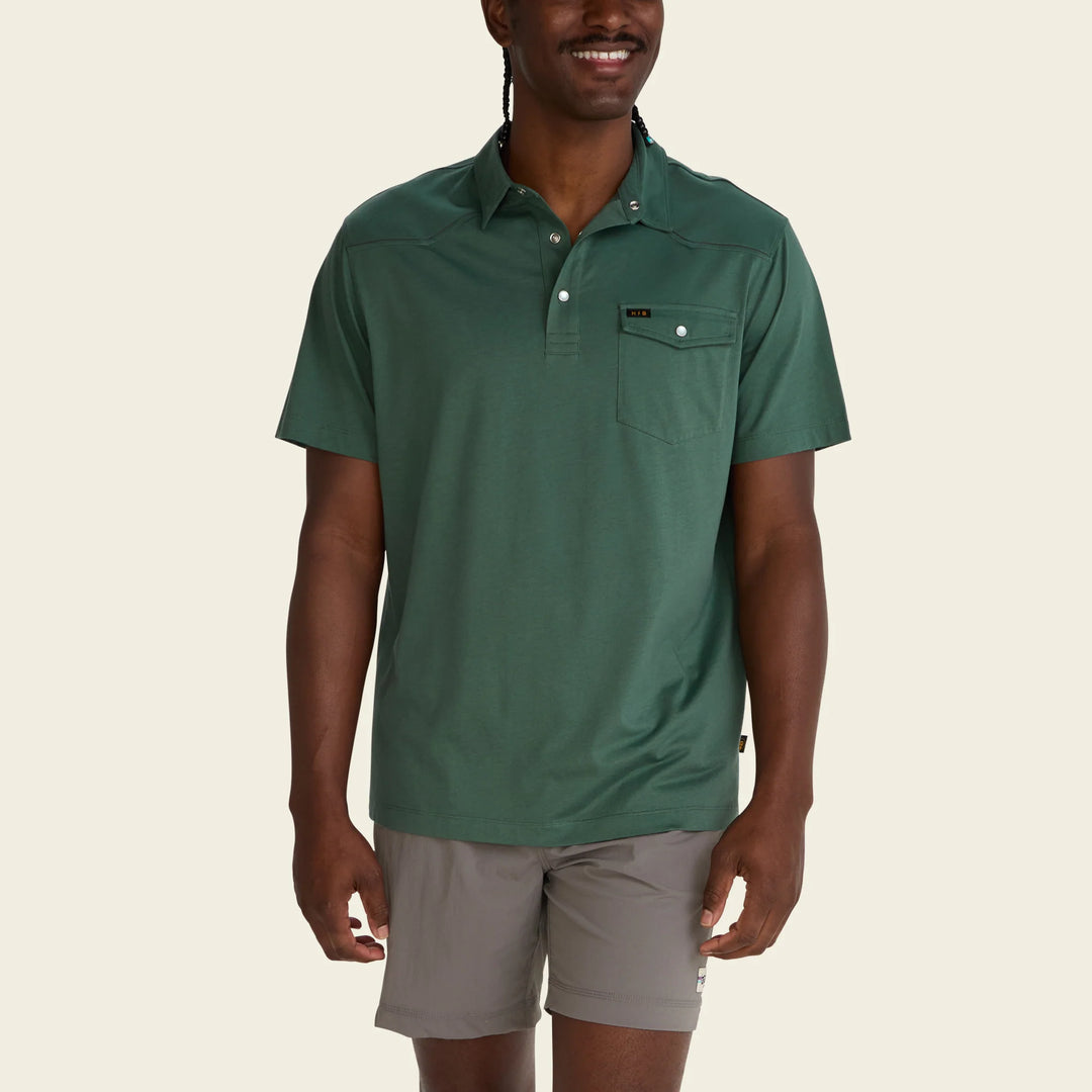 Man wearing a green polo shirt and gray shorts on a beige background