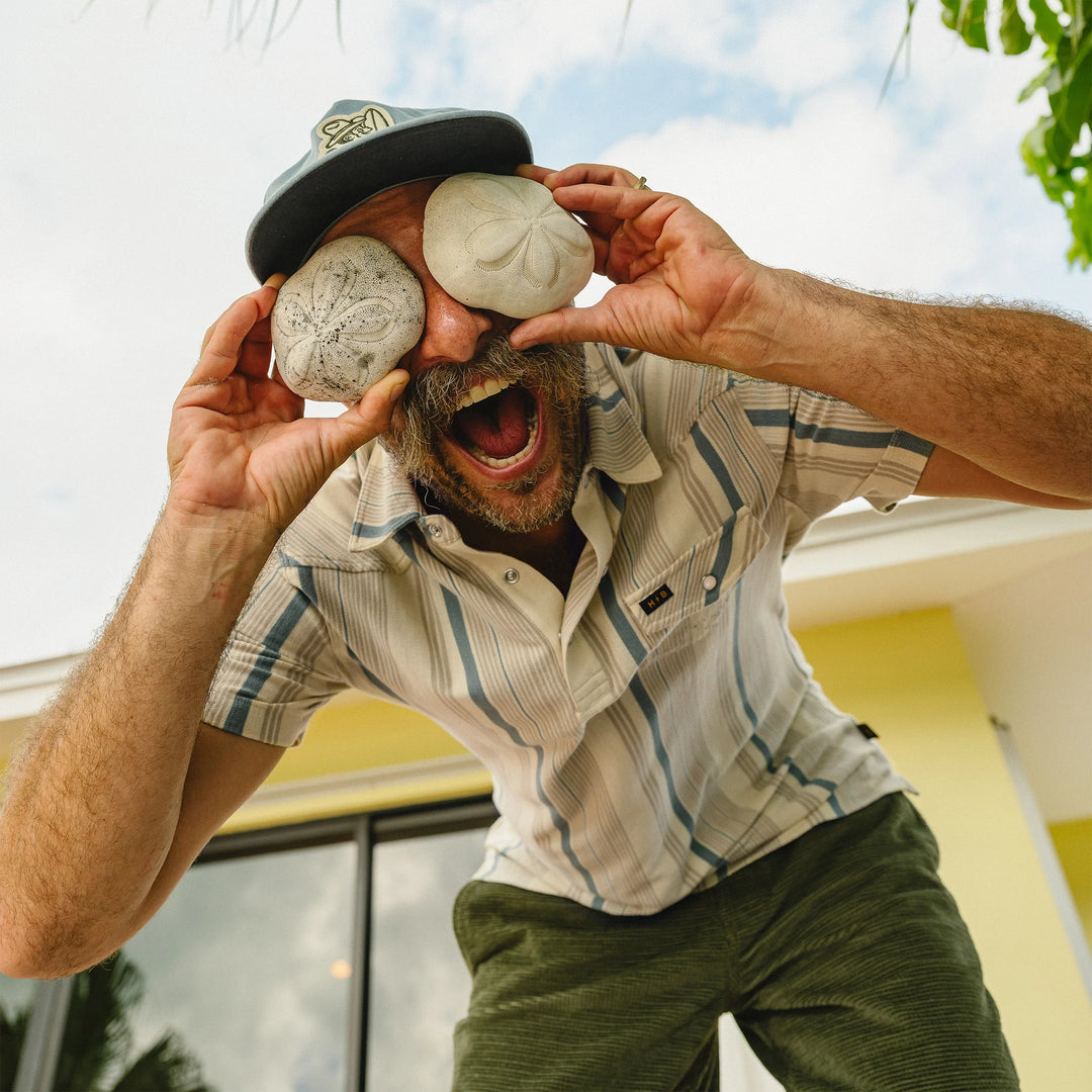 Man holding two stones up to his eyes outdoors with a building in the background