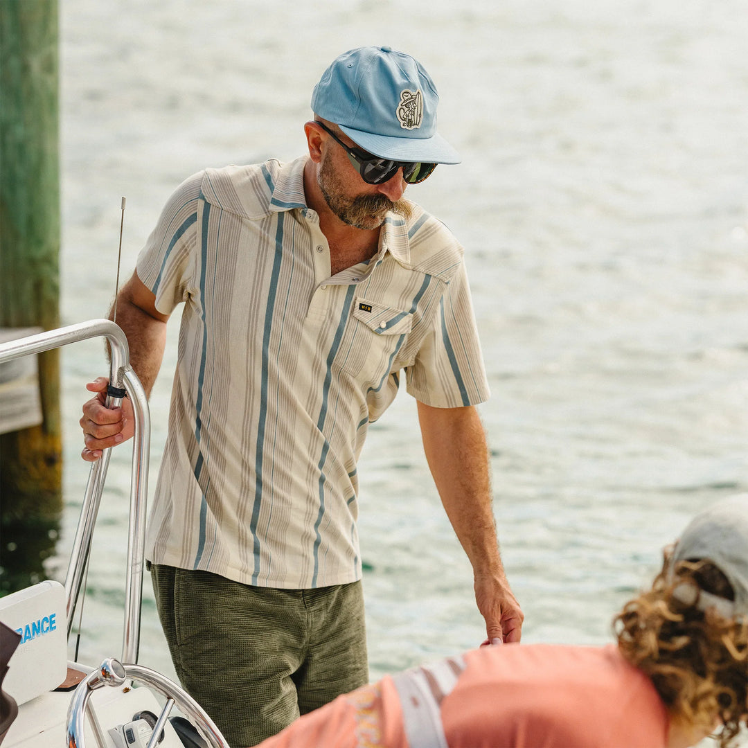 Man on a boat wearing a striped shirt and cap, with water in the background