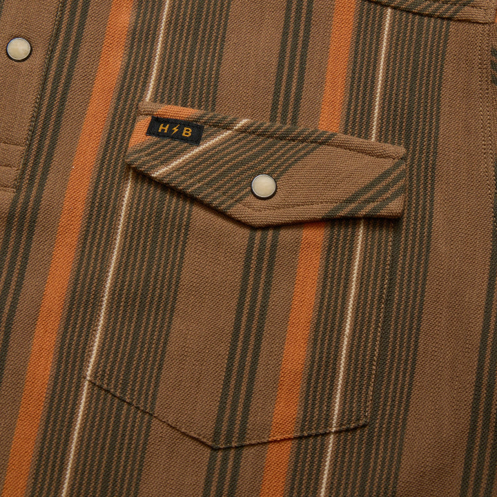 Close-up of a brown and orange striped shirt with a pocket and button, featuring a logo on the chest.