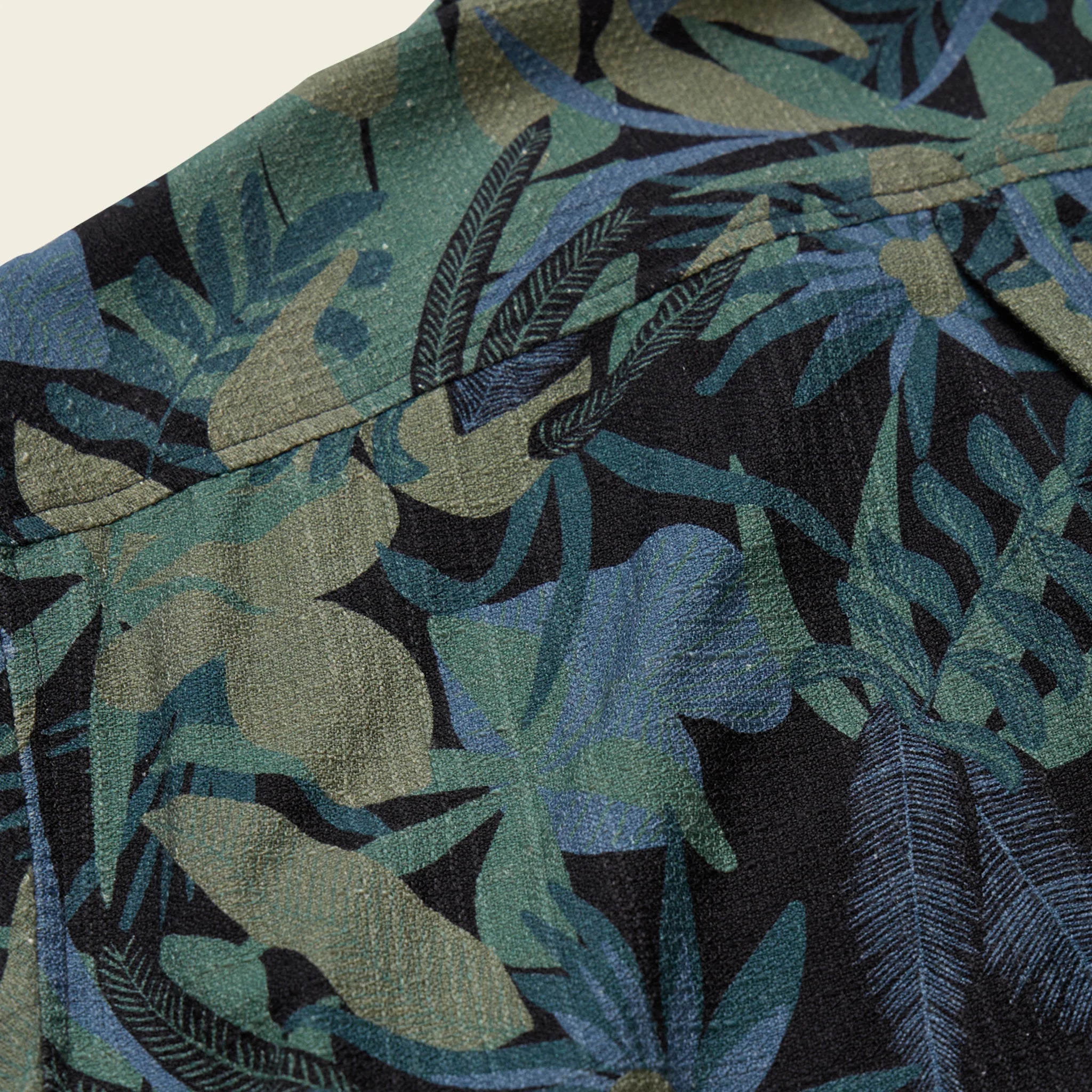 Close-up of a fabric with a tropical leaf pattern in green, blue, and black.