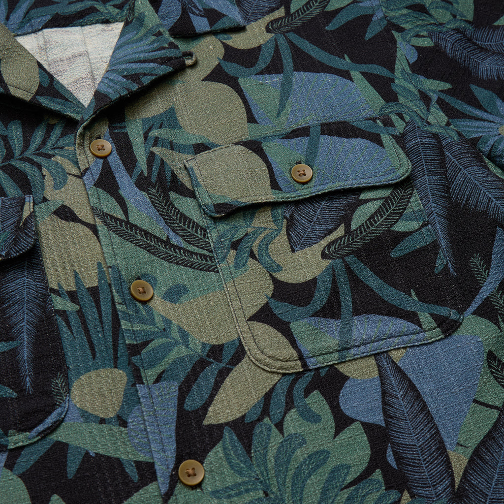 Close-up of a shirt with a tropical leaf pattern in shades of green, blue, and brown.