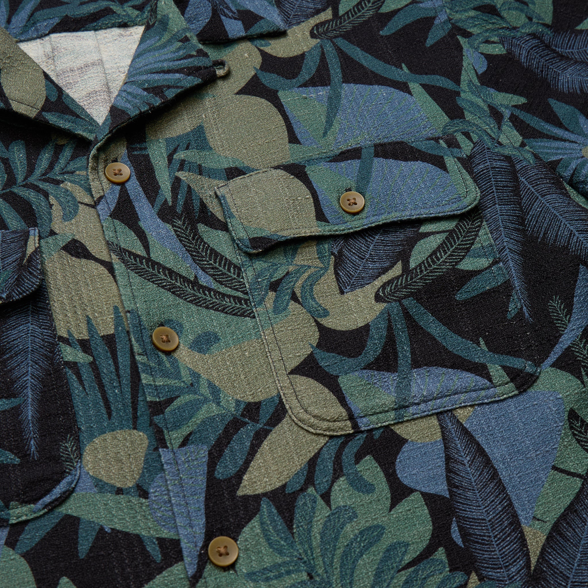 Close-up of a shirt with a tropical leaf pattern in shades of green, blue, and brown.
