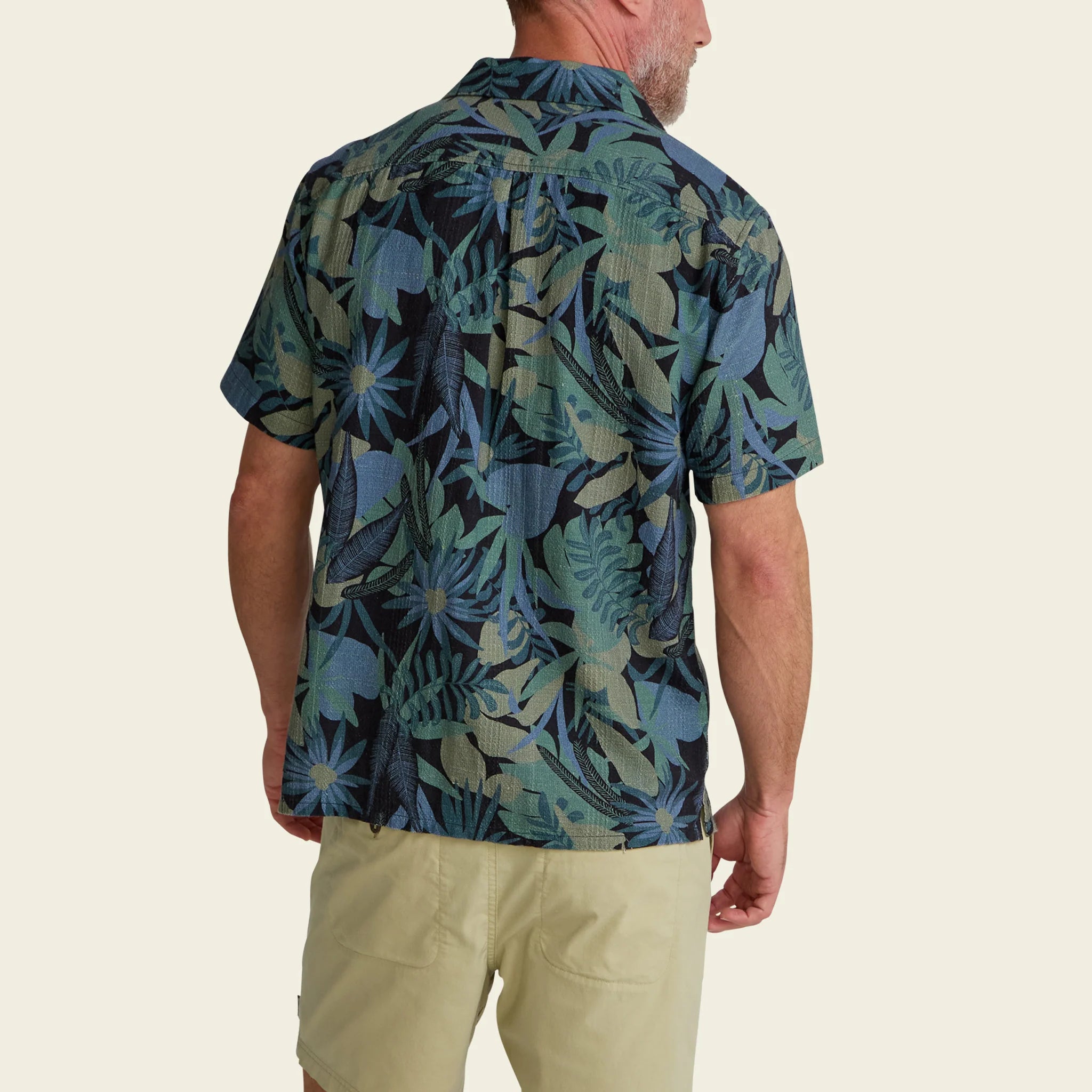 Man wearing a short-sleeve shirt with a tropical leaf pattern on a beige background