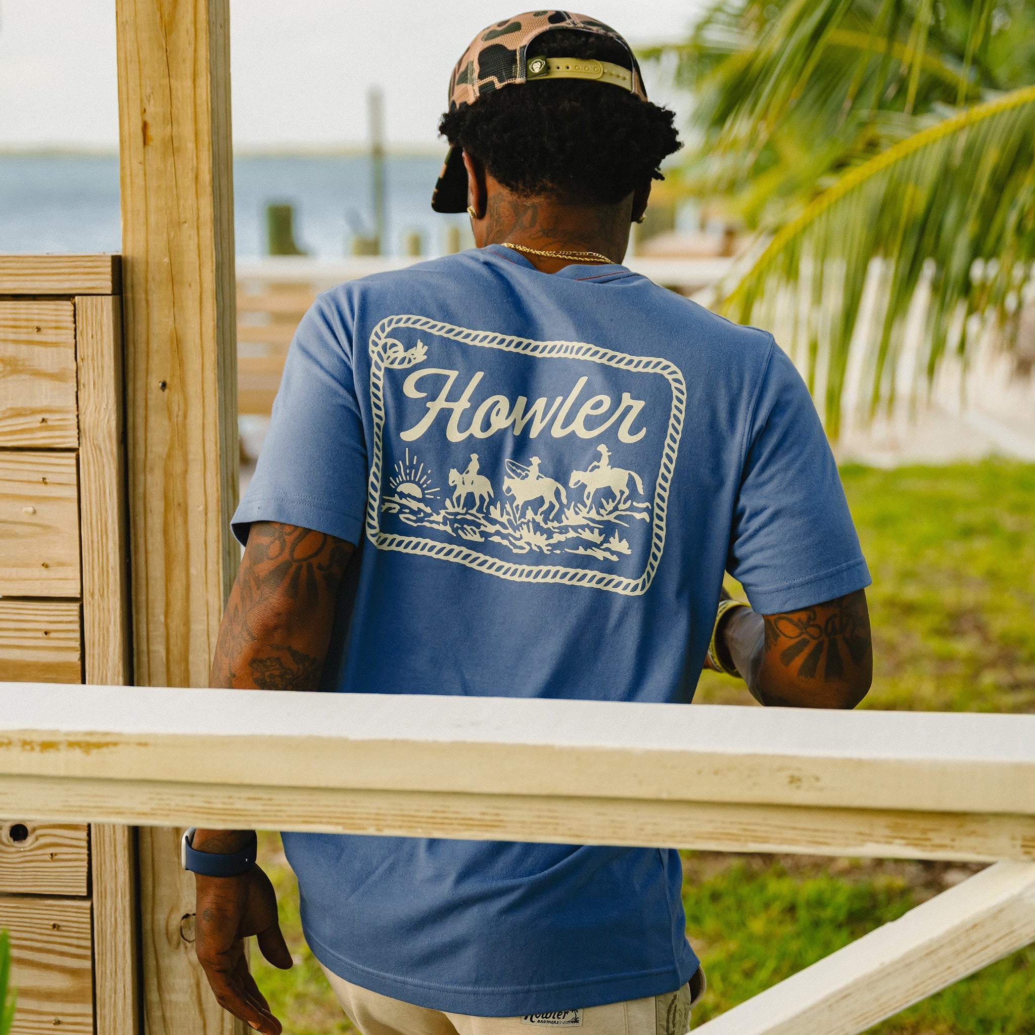 Person wearing a blue 'Howler' t-shirt with a scenic design, standing outdoors.