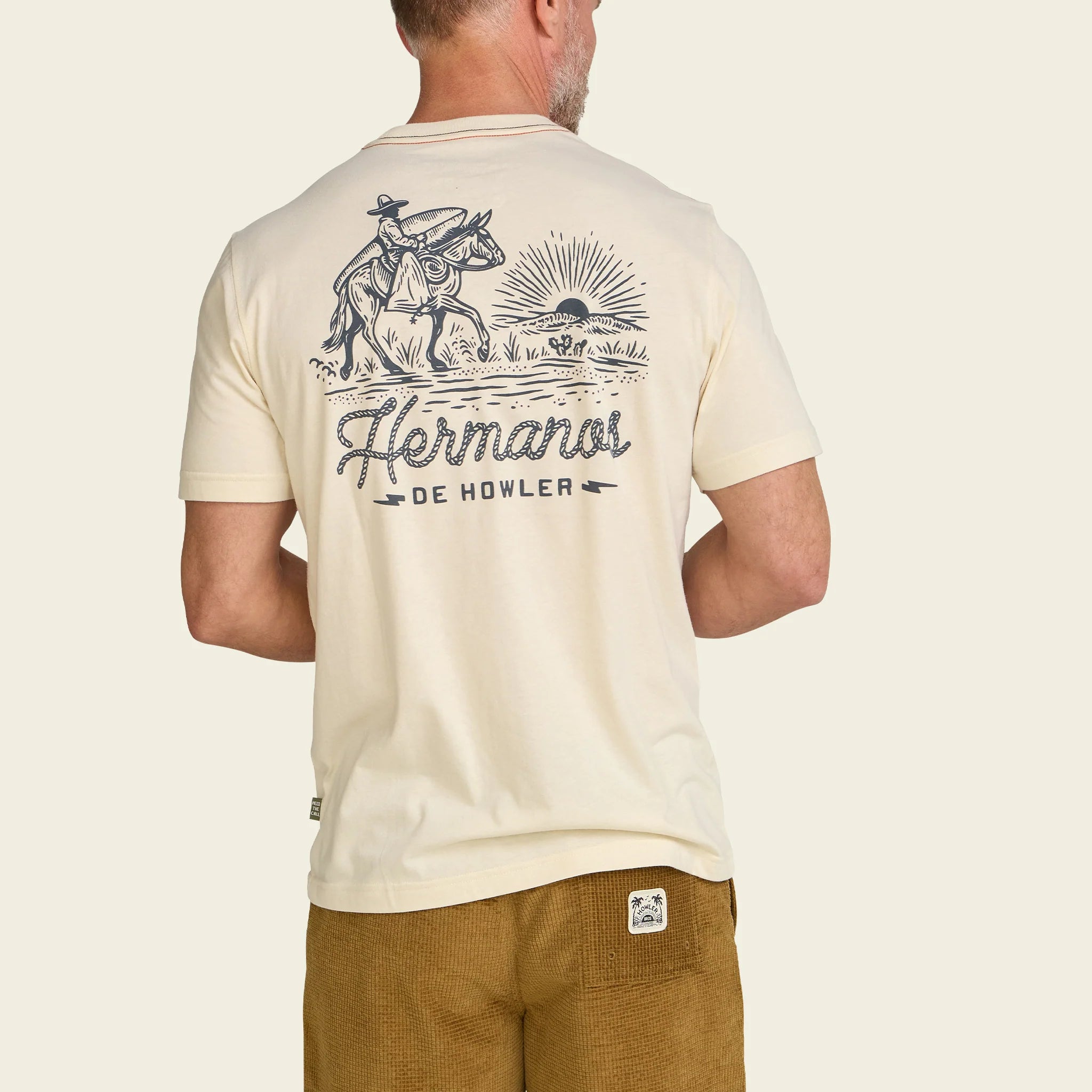 Man wearing a cream t-shirt with a graphic design and text on the back, standing against a plain background.