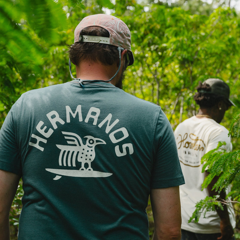 Person wearing a green 'Hermanos' t-shirt in a forest setting
