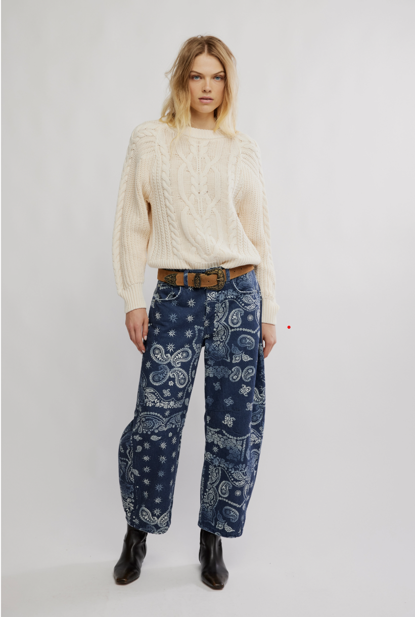 Woman wearing a cream sweater and blue bandana-patterned pants on a white background
