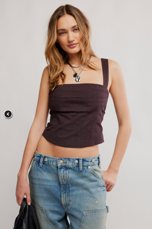 Woman wearing a brown sleeveless top and blue jeans on a plain background
