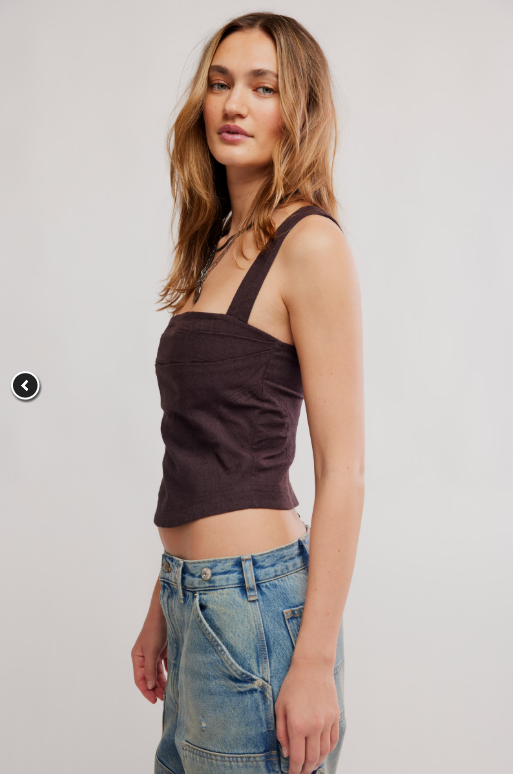 Woman wearing a brown tank top and blue jeans on a plain background