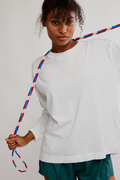 Person wearing a white sweatshirt and green shorts holding a colorful rope against a plain background