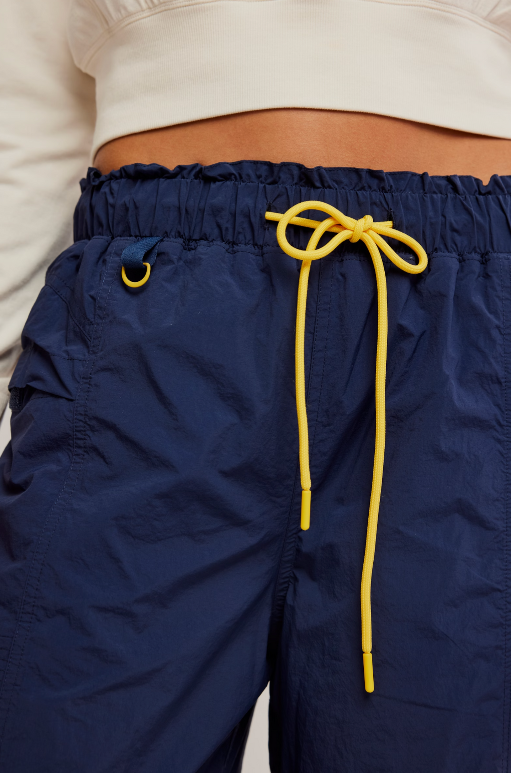 Close-up of a person wearing navy blue lightweight drawstring shorts with a bright yellow drawstring and a matching yellow eyelet detail, paired with a white cropped top.