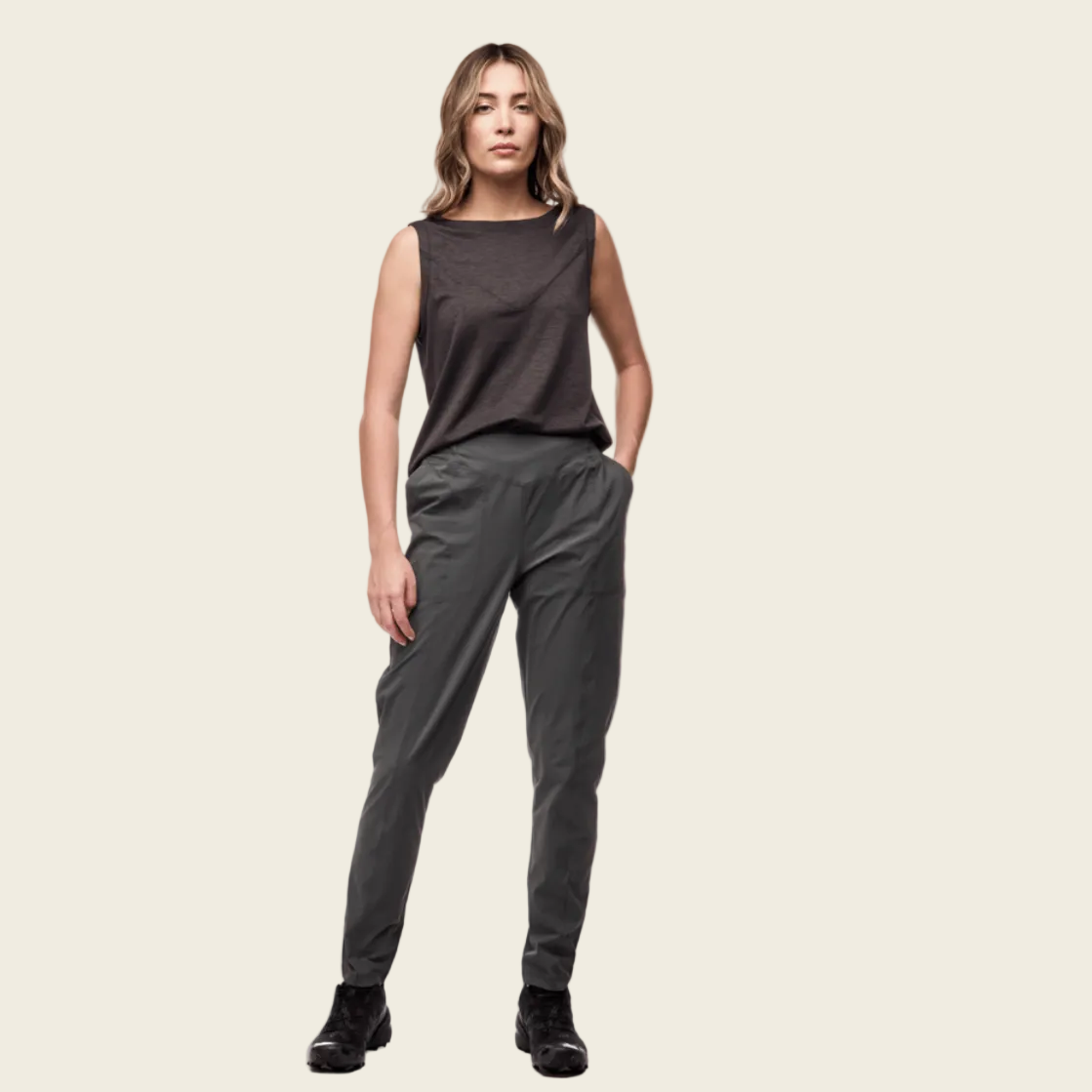 Woman wearing a dark sleeveless top and gray pants on a white background