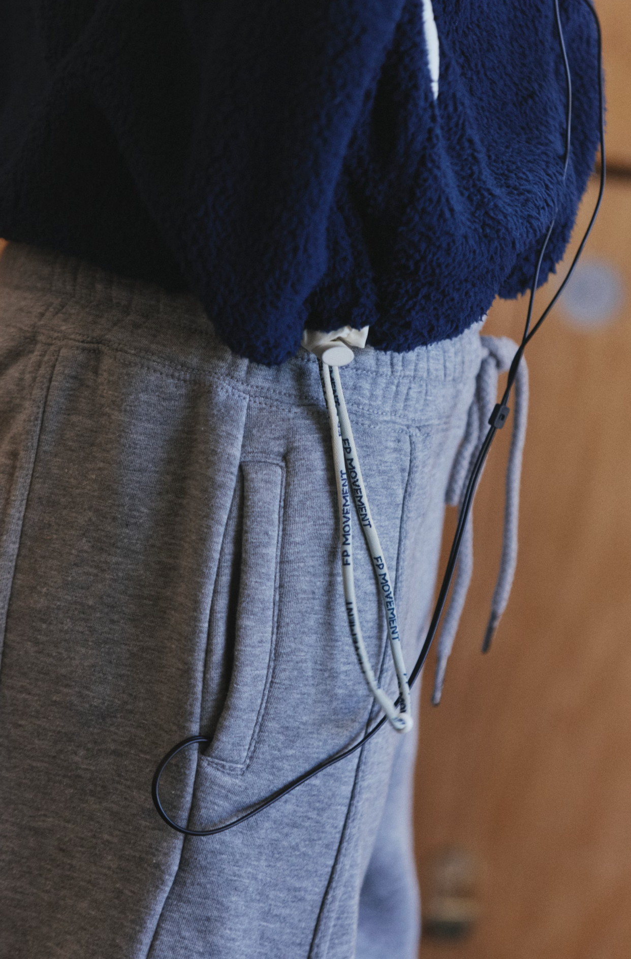 Close-up of a person wearing heather gray drawstring sweatpants and a navy fleece top, with black wired earphones draped around the pocket area.