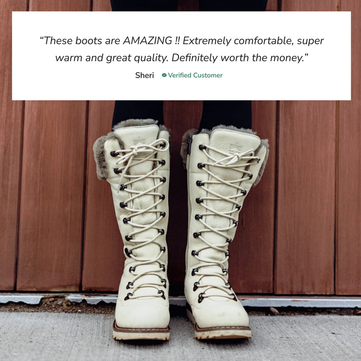 White winter boots with fur lining worn by a person, against a wooden background.