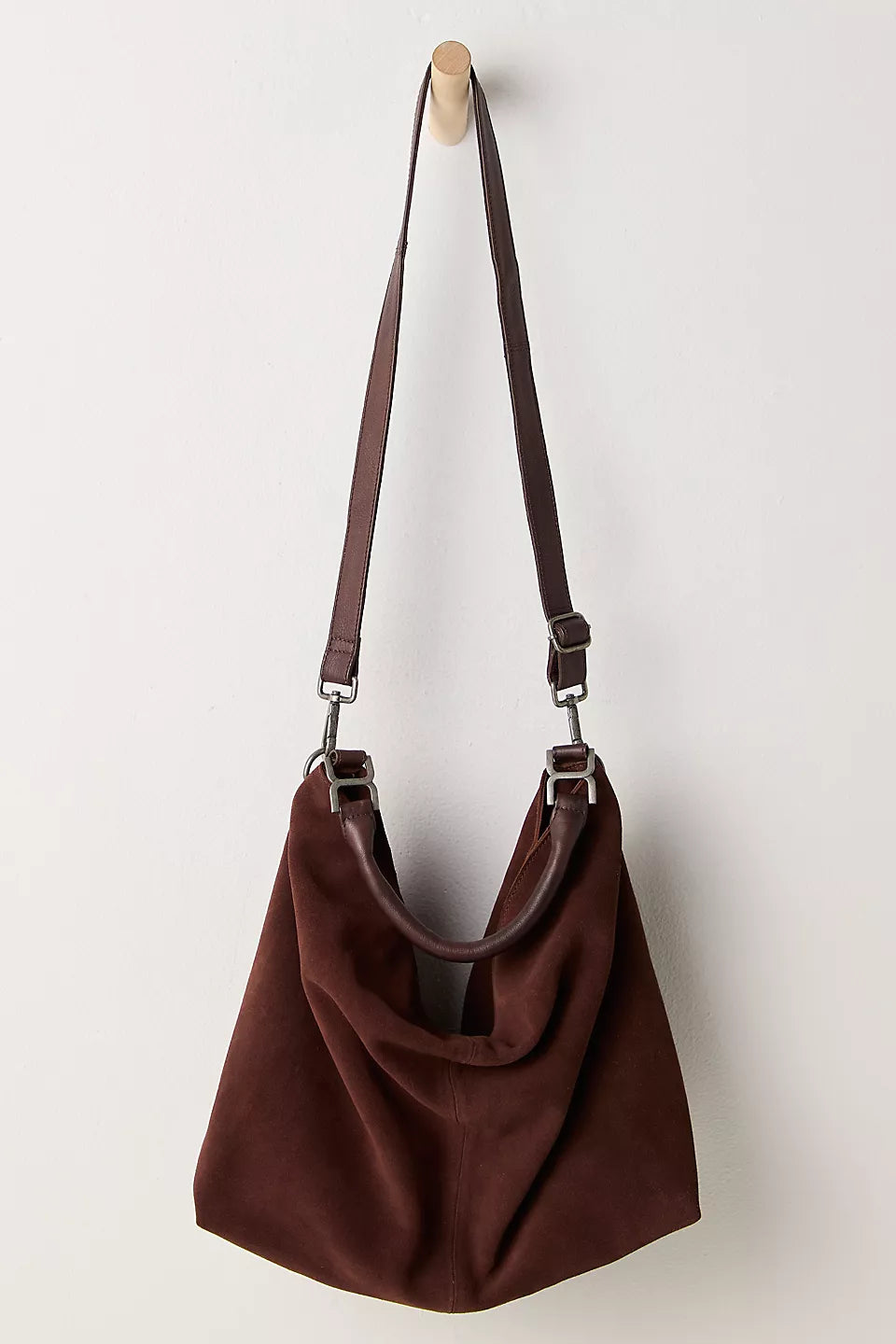 Suzie Suede Slouch Tote in Espresso hanging on a wooden hook by the shoulder strap white background