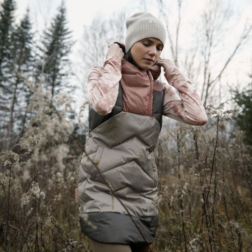 woman in the autumn forest walking wearing a hat and long sleeves with a puffy vest.