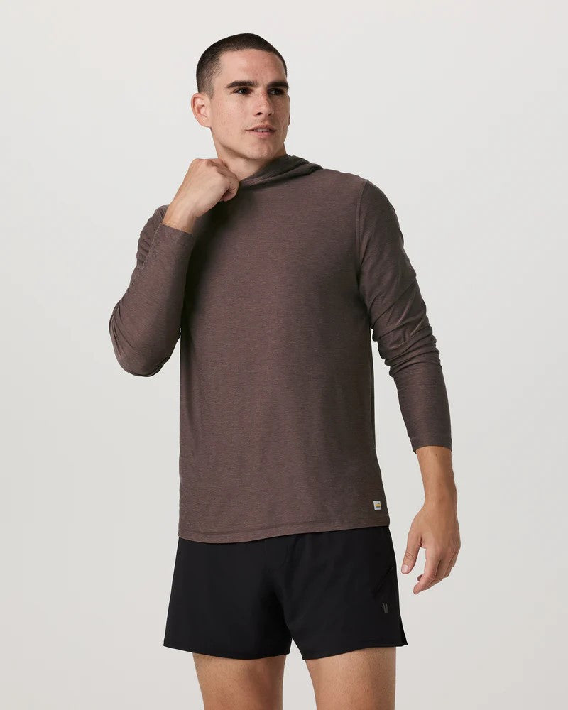 Man wearing a brown long-sleeve shirt and black shorts on a light gray background