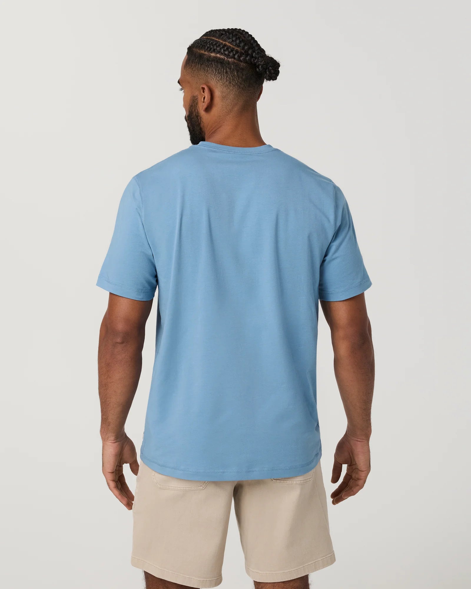 Man wearing a blue t-shirt and beige shorts on a plain background