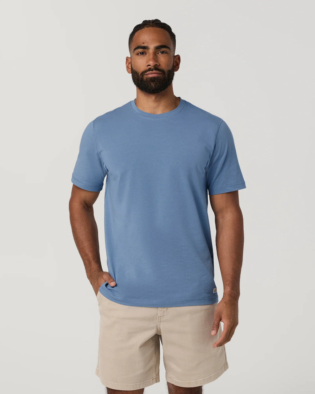 Man wearing a blue t-shirt and beige shorts on a plain background