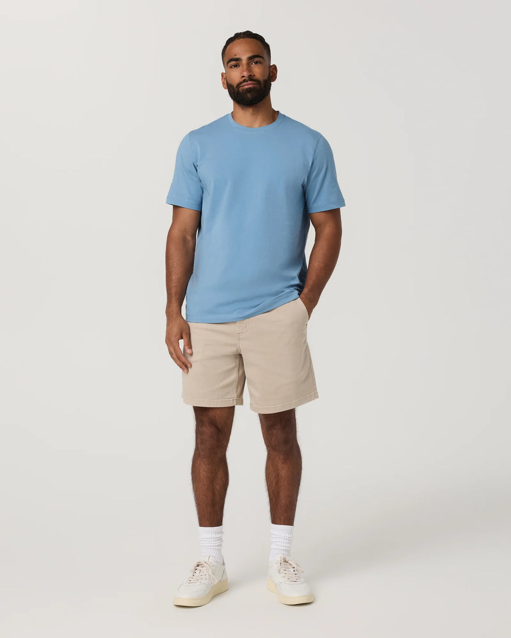 Man wearing a light blue t-shirt and beige shorts on a white background
