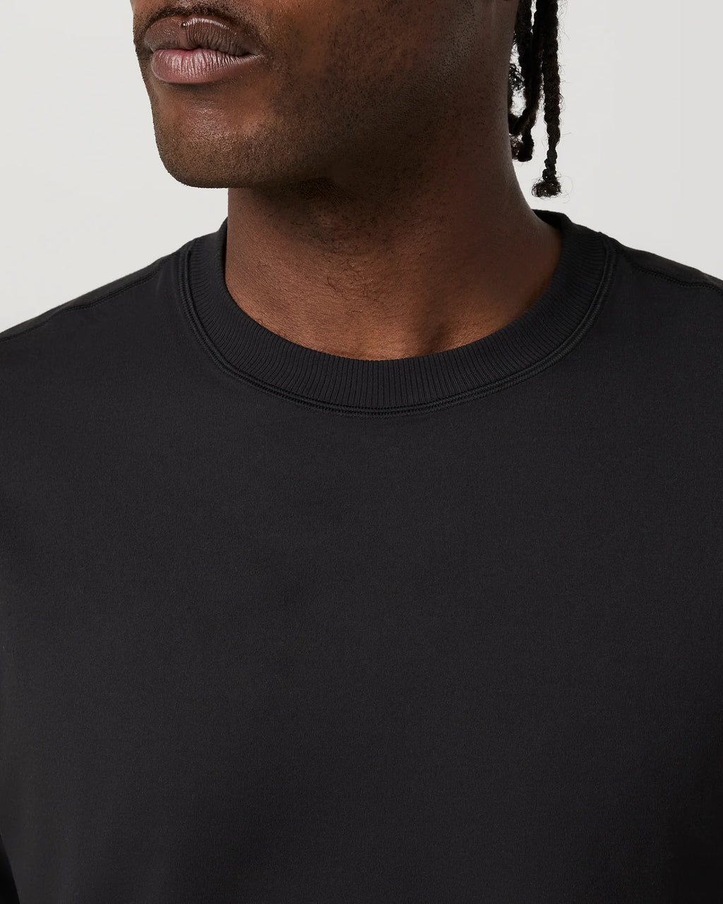 Close-up of a person wearing a plain black crew-neck top against a light neutral background.