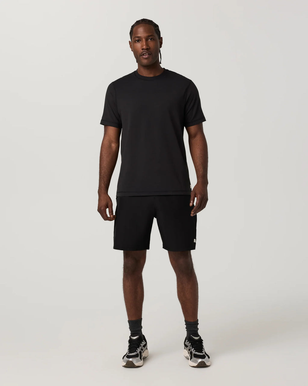 A man modeling a black short-sleeve crewneck t-shirt and black athletic shorts against a light gray studio background.