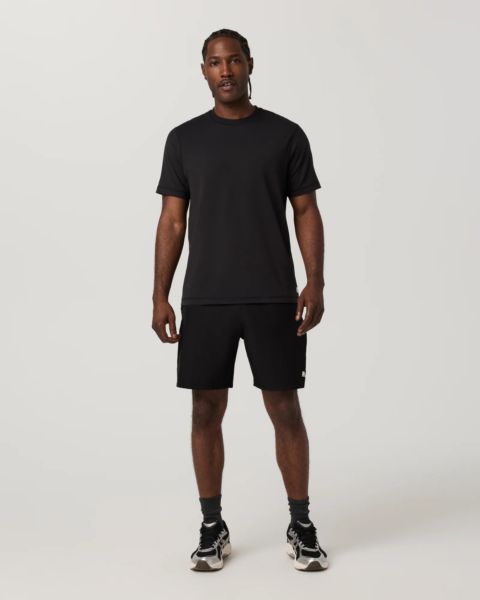 A man modeling a black short-sleeve crewneck t-shirt and black athletic shorts against a light gray studio background.