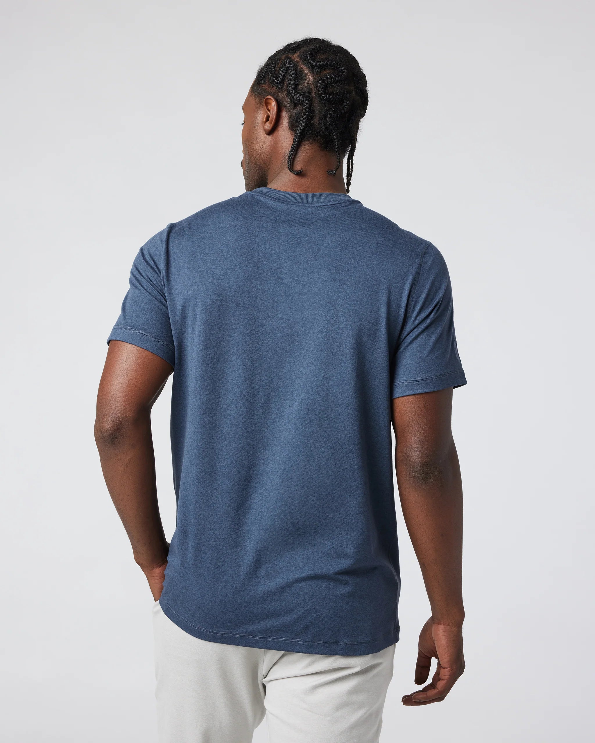 Man wearing a blue t-shirt and white pants against a plain background