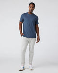 Man wearing a blue t-shirt and white pants against a plain background