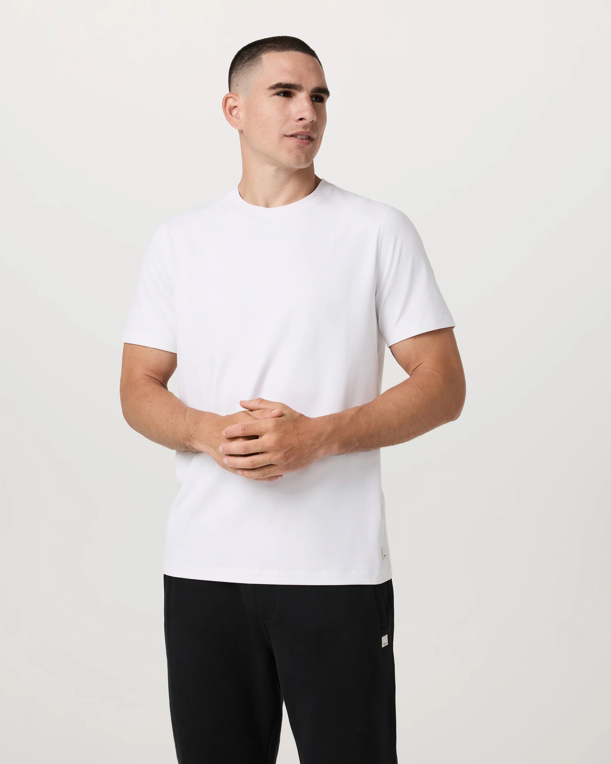 Man wearing a white t-shirt and black pants against a plain background