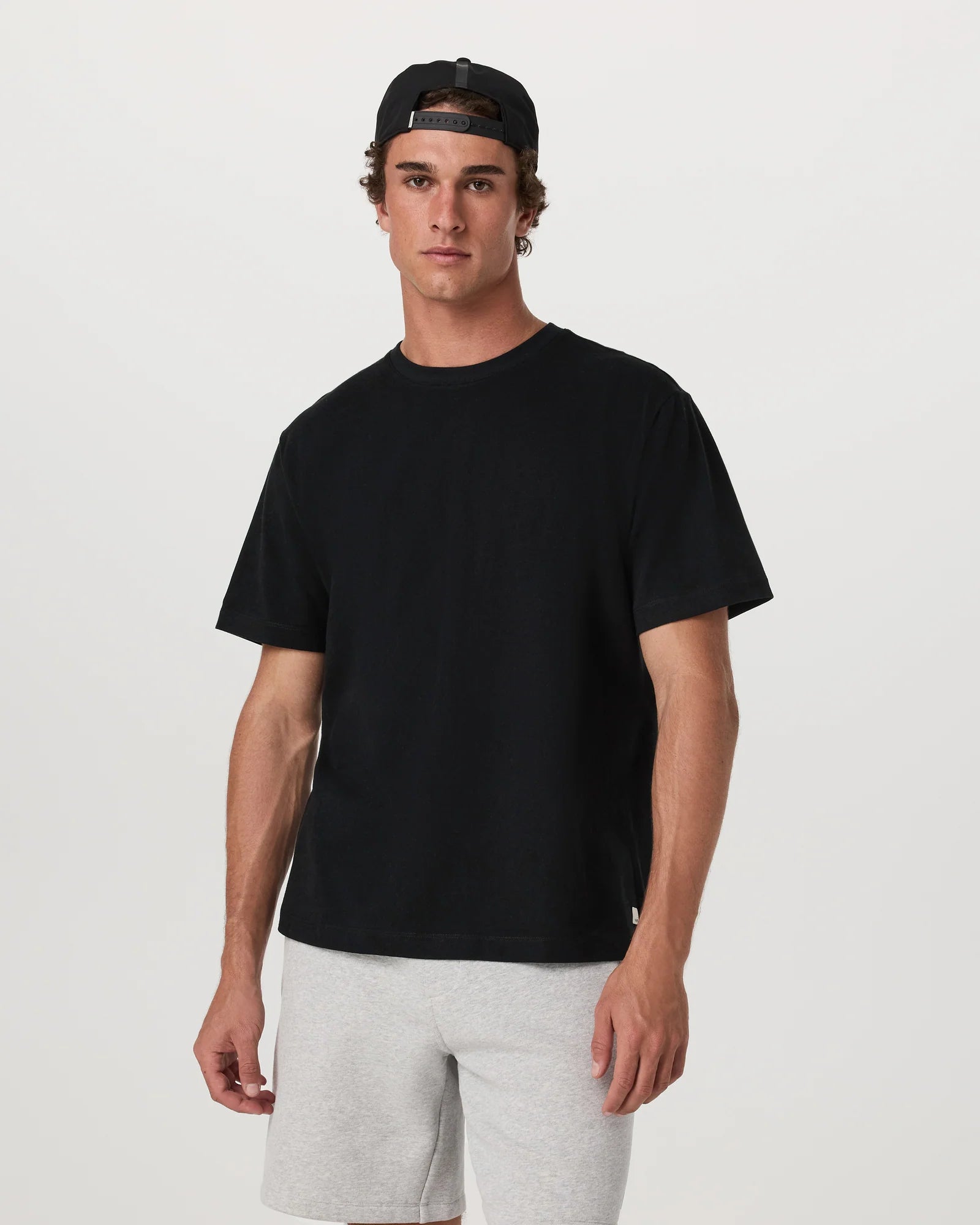 Man wearing a black t-shirt and gray shorts on a white background